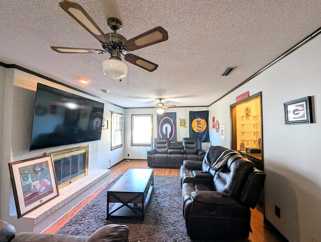 living room with a textured ceiling, ceiling fan, crown molding, hardwood / wood-style flooring, and a fireplace