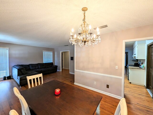 dining room with wood-type flooring, a textured ceiling, and an inviting chandelier