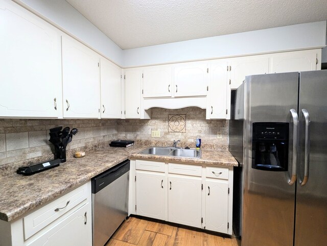 kitchen featuring sink, a textured ceiling, appliances with stainless steel finishes, light hardwood / wood-style floors, and white cabinetry