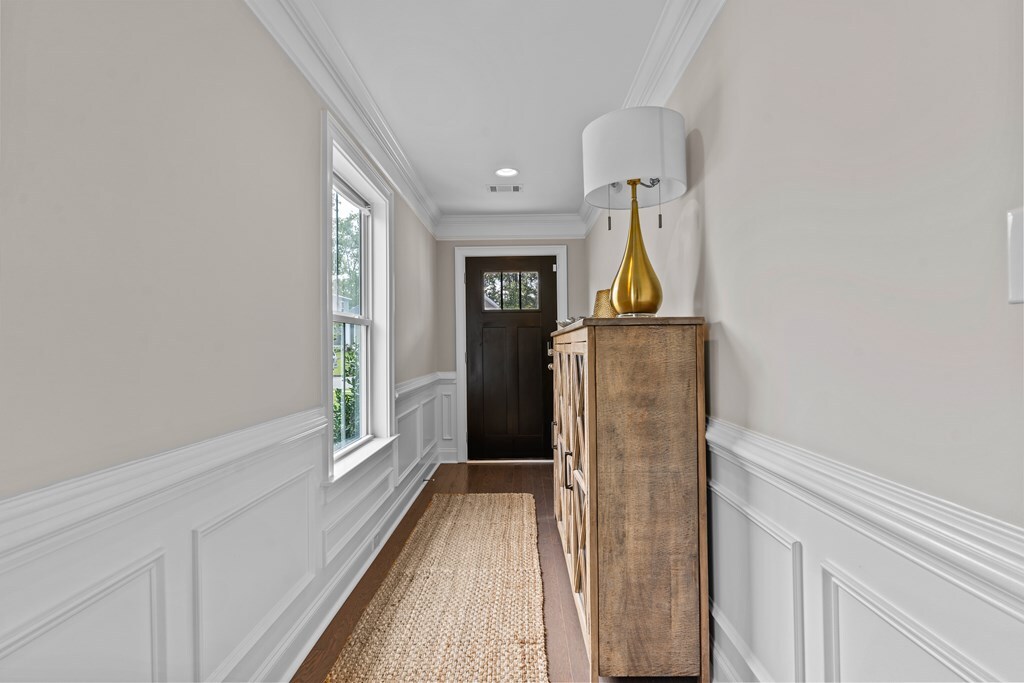doorway to outside featuring a wainscoted wall, a decorative wall, visible vents, crown molding, and dark wood finished floors