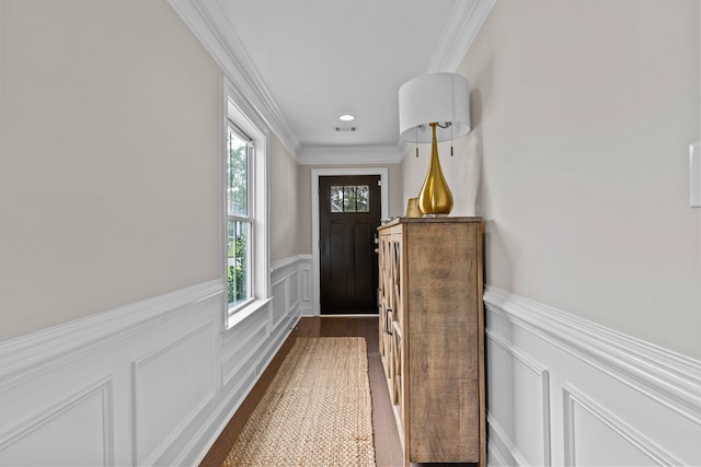 doorway to outside featuring a wainscoted wall, a decorative wall, visible vents, crown molding, and dark wood finished floors