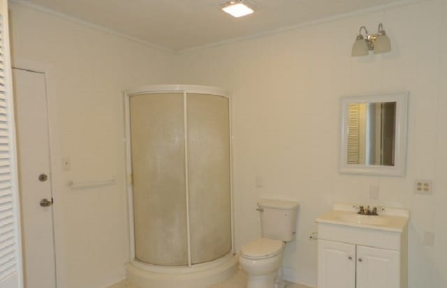 full bathroom featuring vanity, crown molding, toilet, and a shower stall