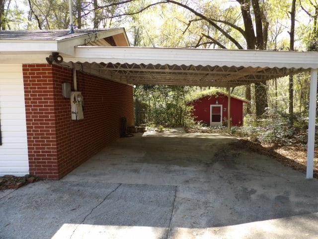 view of parking / parking lot featuring an attached carport, driveway, and a storage unit