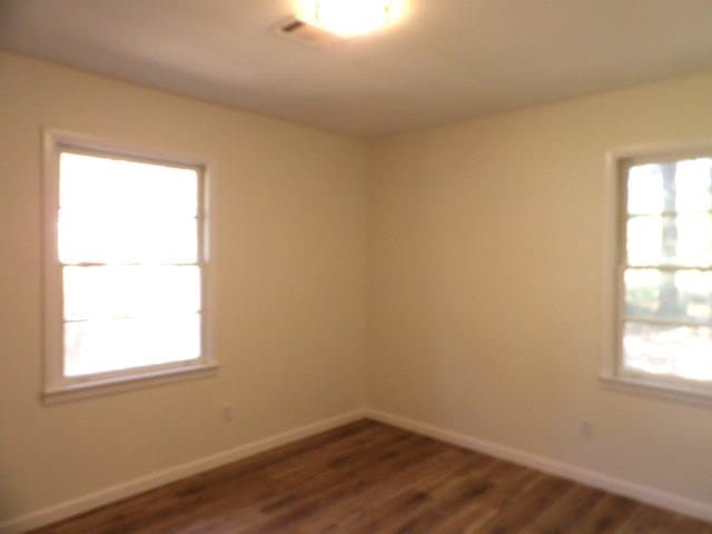 unfurnished room featuring dark wood finished floors, a wealth of natural light, and baseboards