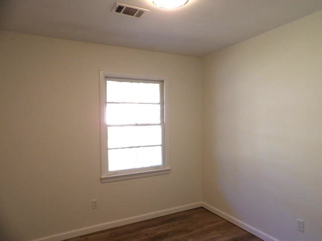 spare room with dark wood-style floors, baseboards, and visible vents