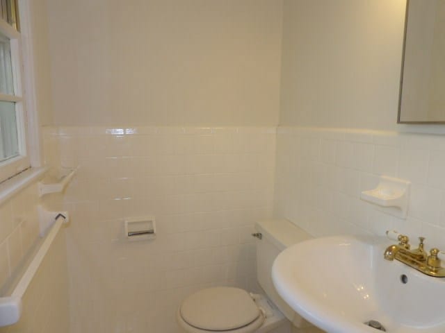 half bathroom with tile walls, a wainscoted wall, a sink, and toilet
