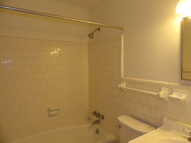 bathroom featuring tile walls, toilet, bathing tub / shower combination, and a sink