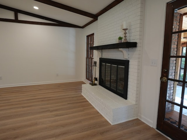 unfurnished living room featuring lofted ceiling with beams, a fireplace, a healthy amount of sunlight, and wood-type flooring