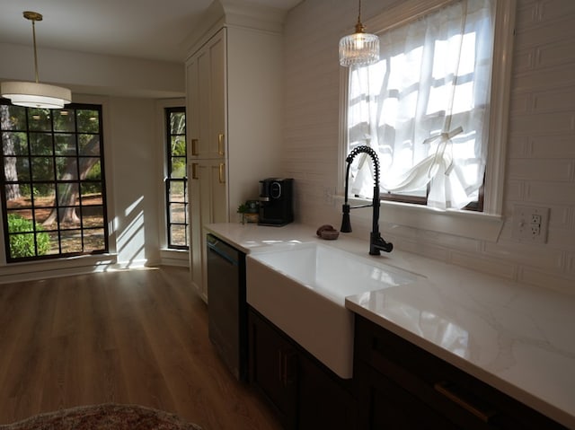 kitchen featuring dishwasher, sink, dark wood-type flooring, light stone counters, and pendant lighting