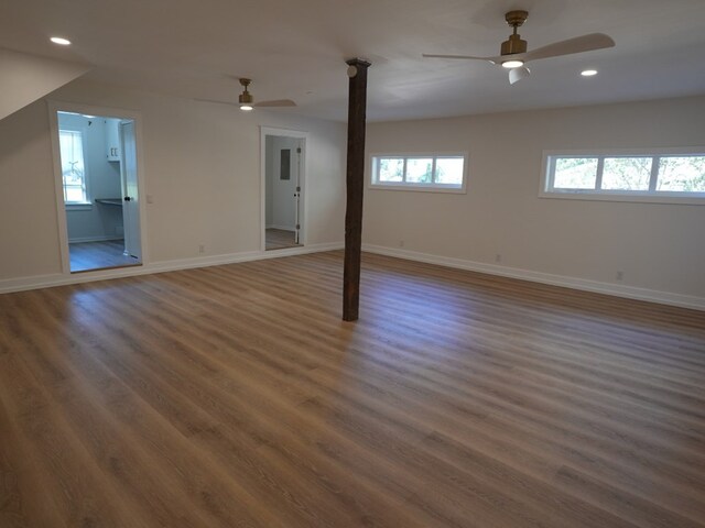 basement featuring ceiling fan, dark wood-type flooring, and a healthy amount of sunlight