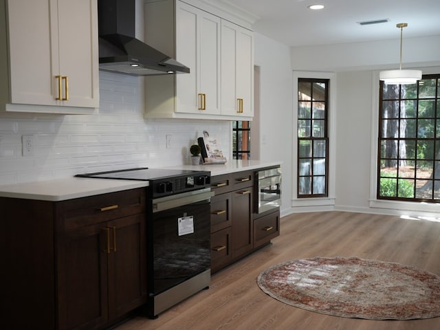 kitchen with decorative backsplash, appliances with stainless steel finishes, light wood-type flooring, wall chimney range hood, and white cabinetry