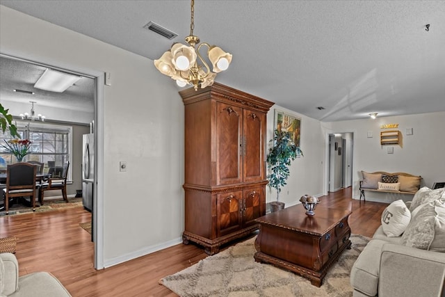 living room with baseboards, visible vents, an inviting chandelier, a textured ceiling, and light wood-style floors