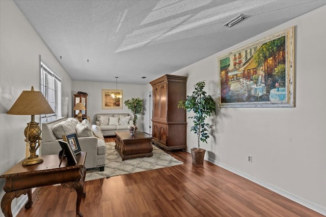 living area with visible vents, a textured ceiling, baseboards, and wood finished floors