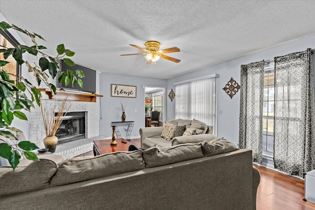 living area with a brick fireplace, a textured ceiling, a ceiling fan, and wood finished floors