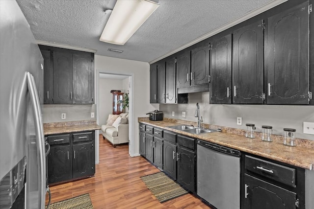 kitchen with light wood-style flooring, dark cabinetry, stainless steel appliances, and a sink