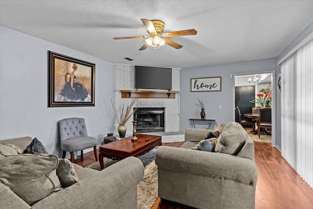 living room featuring visible vents, a textured ceiling, light wood-style floors, a fireplace, and ceiling fan with notable chandelier