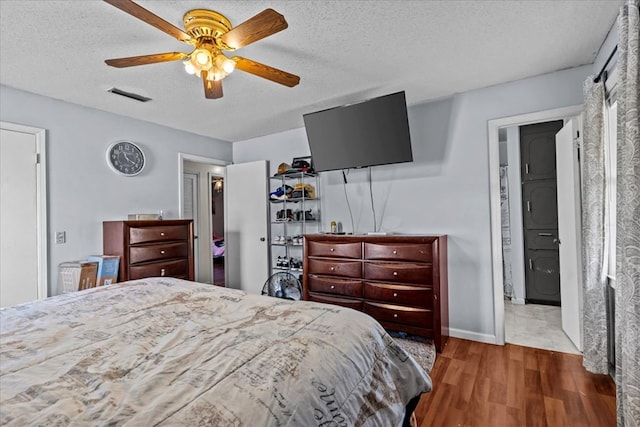 bedroom featuring a textured ceiling, ceiling fan, wood finished floors, visible vents, and baseboards