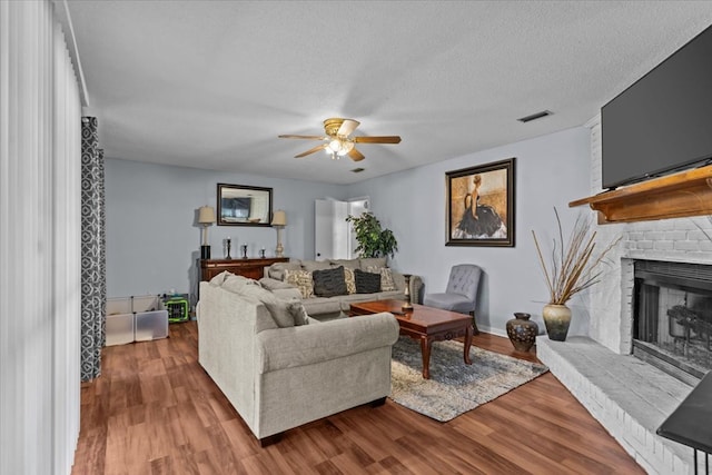 living area with visible vents, a fireplace, a textured ceiling, and wood finished floors