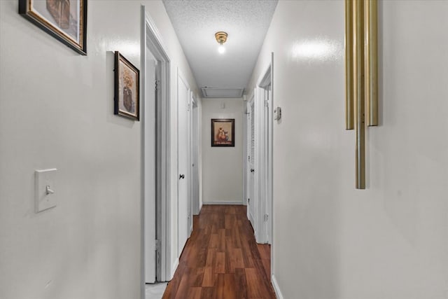 hall with attic access, baseboards, a textured ceiling, and wood finished floors