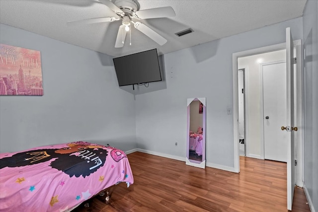 bedroom with a textured ceiling, ceiling fan, wood finished floors, visible vents, and baseboards