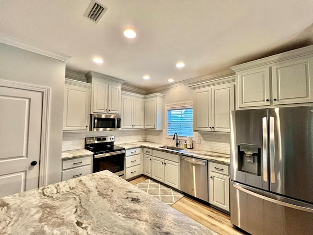 kitchen with sink, crown molding, light wood-type flooring, tasteful backsplash, and stainless steel appliances