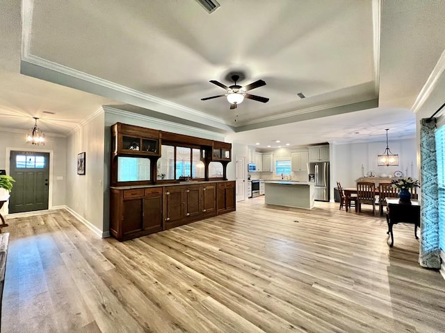 living room with ornamental molding, ceiling fan with notable chandelier, light hardwood / wood-style floors, and a tray ceiling