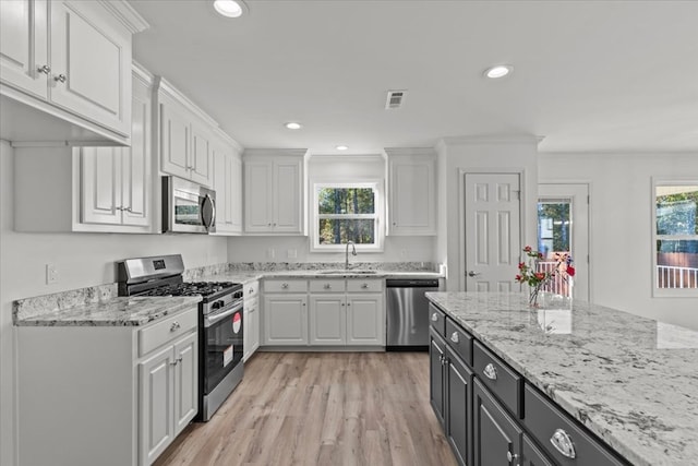 kitchen with sink, light stone countertops, appliances with stainless steel finishes, light hardwood / wood-style floors, and white cabinetry