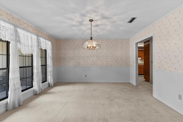 carpeted spare room featuring a notable chandelier, ornamental molding, and a textured ceiling