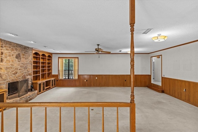 interior space with ceiling fan, a stone fireplace, wood walls, a textured ceiling, and light carpet