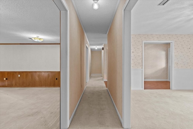 corridor with light carpet, a textured ceiling, and wooden walls