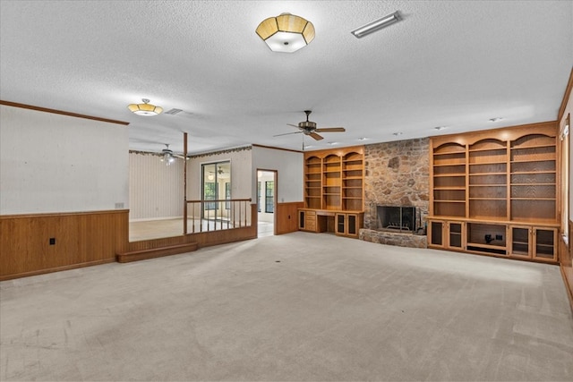 unfurnished living room featuring carpet flooring, wooden walls, a fireplace, and a textured ceiling