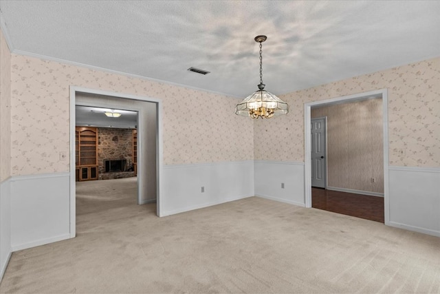 carpeted empty room featuring crown molding, a stone fireplace, a textured ceiling, and a chandelier