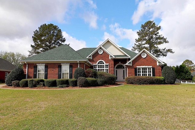 view of front of property featuring a front yard, brick siding, and a shingled roof