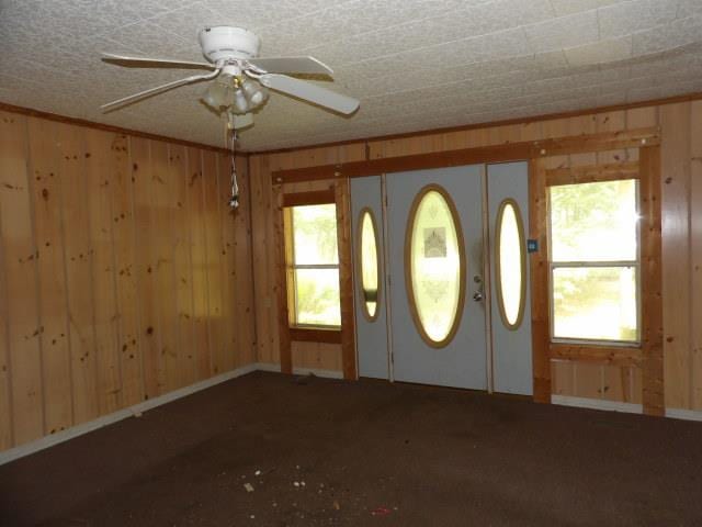 interior space featuring ceiling fan and wood walls