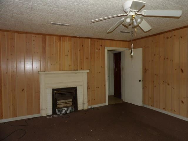 1011 Sunset Blvd, Elba, AL 36323 - unfurnished living room with wood walls, a fireplace, carpet floors, and a ceiling fan