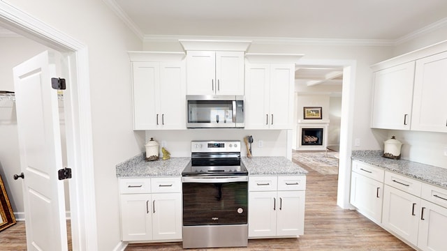 kitchen featuring light stone countertops, light wood-type flooring, ornamental molding, white cabinetry, and stainless steel appliances