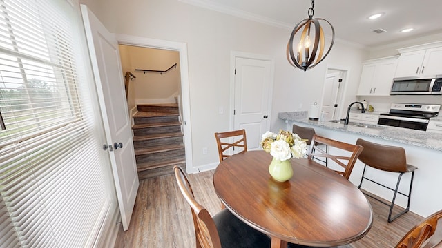 dining space with light wood-type flooring, a notable chandelier, crown molding, and sink