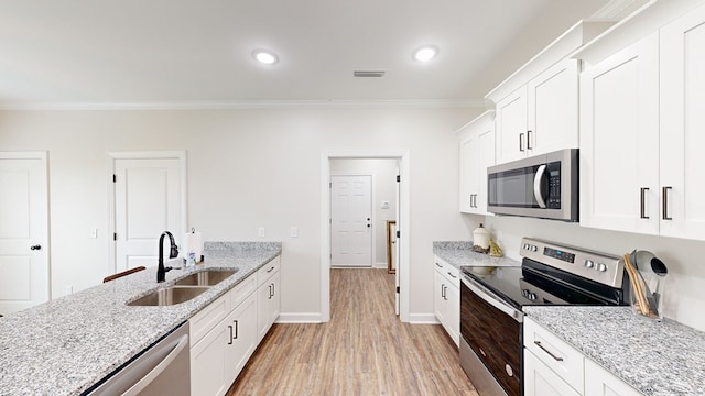 kitchen with ornamental molding, stainless steel appliances, sink, light hardwood / wood-style floors, and white cabinetry