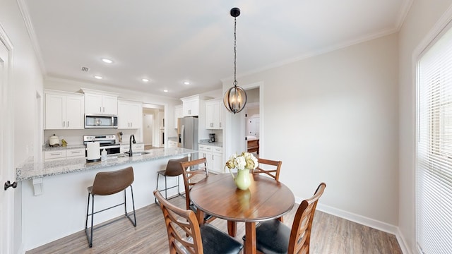 dining space with ornamental molding, sink, and light hardwood / wood-style flooring