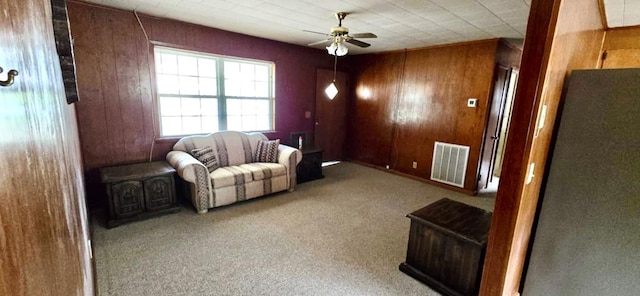 living area with visible vents, wooden walls, a ceiling fan, and carpet flooring