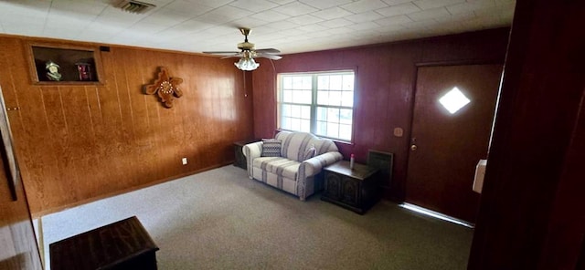 living area featuring wooden walls, carpet, visible vents, and ceiling fan