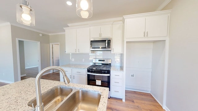 kitchen featuring white cabinets, a sink, appliances with stainless steel finishes, crown molding, and decorative backsplash