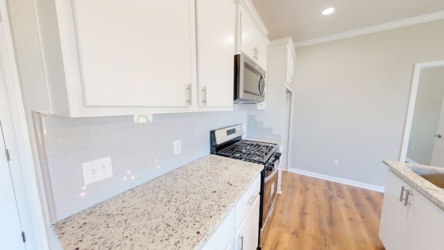 kitchen with ornamental molding, white cabinetry, appliances with stainless steel finishes, light stone counters, and light wood finished floors
