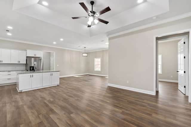 unfurnished living room with ornamental molding, a tray ceiling, dark wood-type flooring, and baseboards