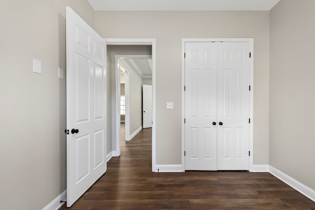 unfurnished bedroom with a closet, baseboards, and dark wood-style flooring