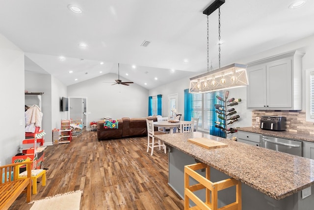 kitchen featuring light stone counters, a center island, lofted ceiling, stainless steel dishwasher, and wood finished floors