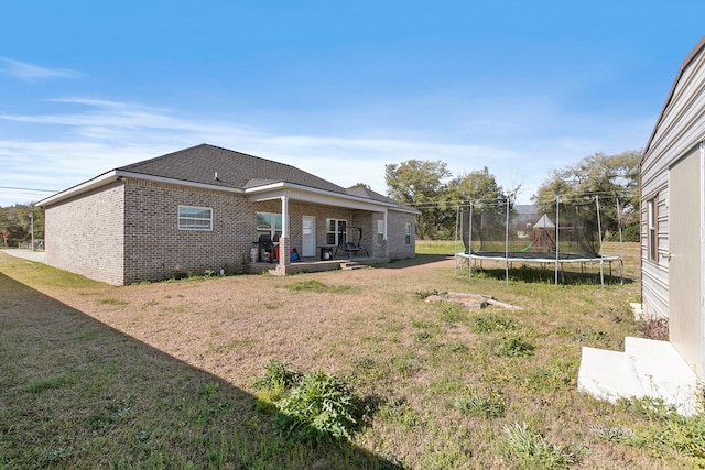 rear view of property featuring a patio area, a trampoline, a lawn, and brick siding