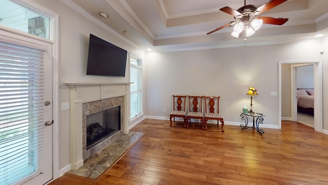 living area with ornamental molding, a raised ceiling, light hardwood / wood-style floors, a fireplace, and ceiling fan