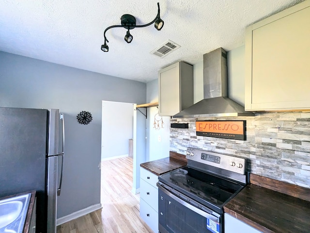 kitchen featuring light wood-type flooring, backsplash, wall chimney exhaust hood, a textured ceiling, and stainless steel appliances