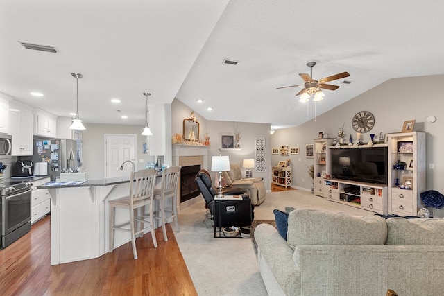 living room featuring ceiling fan, a tiled fireplace, light hardwood / wood-style flooring, and lofted ceiling